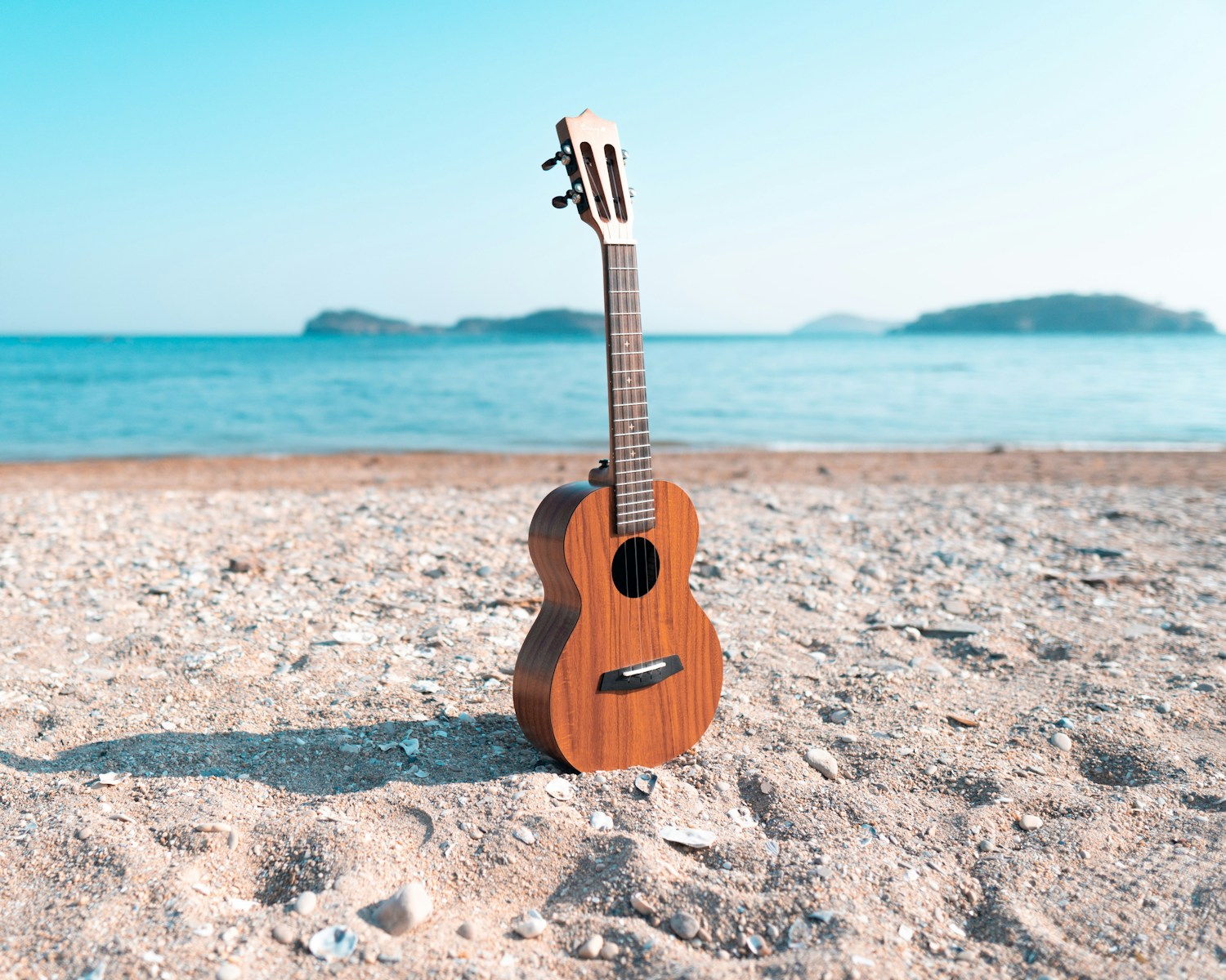 a wooden guitar sitting on top of a sandy beach